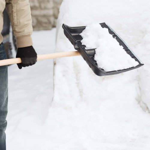 winter and cleaning concept - closeup of man shoveling snow from driveway