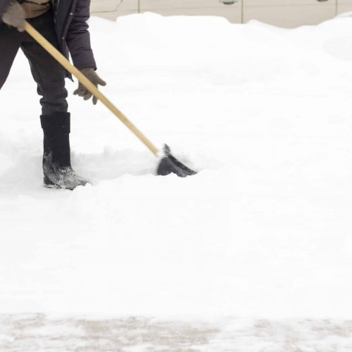 A man in felt boots, with a shovel in his hands, removes snow from the sidewalk after a snowfall.